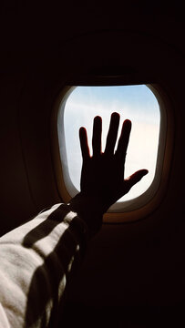 Silhouette of a man's outstretched hand touching an aircraft window