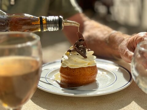 Close-up of a man sitting outdoors pouring rum on a rum baba (baba au rhum) dessert