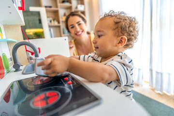 Toddler boy playing with toy kitchen while mother watches