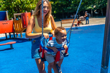 Happy mother pushing her toddler son on a swing at the playground