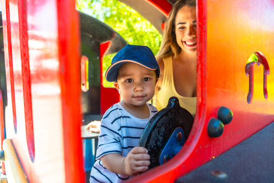 Little boy driving toy train with mother watching at playground - Powered by Adobe