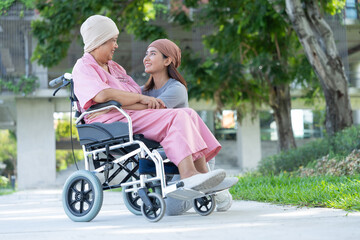 Asian careful caregiver or nurse and woman with cancer is sitting in a wheelchair. in the garden. Concept of happy retirement with care from a caregiver and Savings and senior health insurance.