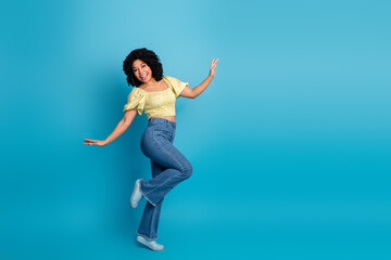 Obraz premium Young cheerful woman in trendy casual clothing dancing joyfully against a vibrant blue background with upbeat energy