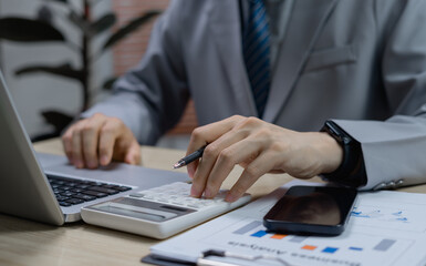Businessman or accountant calculating with calculator and reviewing analytic reports, illustrating financial planning, accounting processes, and business management concepts.