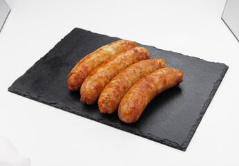 Four golden brown sausages arranged on a dark slate board offer a hearty, savory bite. Ideal for casual dining, barbecues, or menu photography in food and restaurant contexts.