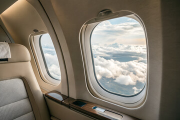 Obraz premium Aerial view of clouds and sky through airplane window of private jet. Peaceful and luxury travel concept with comfort and freedom atmosphere.