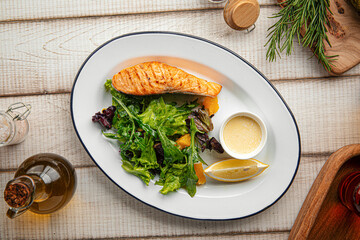 Juicy grilled salmon fillet served with fresh leafy greens and creamy sauce on a white plate