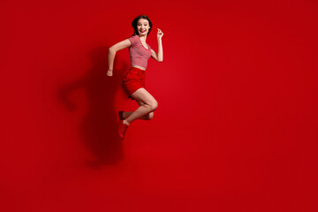 Smiling woman jumping in a dynamic pose on a red background wearing casual attire