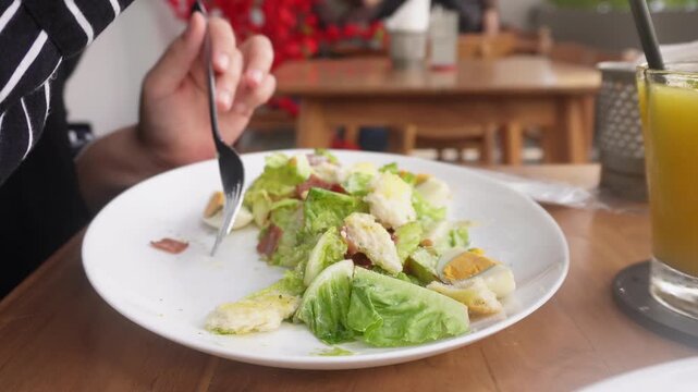  A woman eating Caesar Salad at restaurant. Served with crisp romaine lettuce, eggs, smoked beef, crunchy croutons, parmesan cheese, and a light Caesar dressing