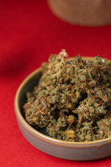 Dry medical marijuana buds in a ceramic saucer on a red background