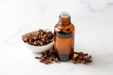 Close up glass bottle of essential clove oil and cloves in wooden spoon on rustic background. Herbs...