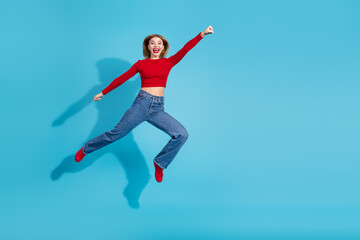 Fototapeta premium Energetic young woman in casual attire leaping joyfully against a vibrant blue background celebrating happiness