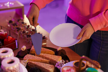 Woman taking delicious dessert from buffet table, closeup