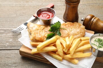 British Traditional Fish and chips served with sauces on wooden table, closeup