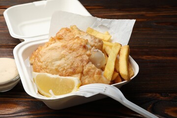 British Traditional Fish and chips with lemon and sauce on wooden table, closeup