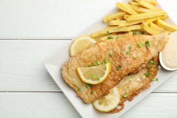 British Traditional Fish and chips with sauce, lemon and green onion on white wooden table, top view