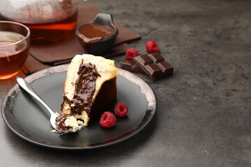 Piece of delicious Basque cheesecake with chocolate sauce, raspberries and tea on grey table, closeup. Space for text