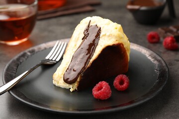 Piece of delicious Basque cheesecake with chocolate sauce, raspberries and tea on grey table, closeup