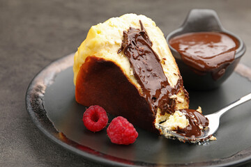 Piece of delicious Basque cheesecake with chocolate sauce and raspberries on grey table, closeup