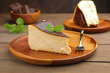 Pieces of delicious Basque cheesecake with mint and chocolate on wooden table, closeup