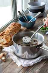 A hand holding a ladle of freshly made cream of mushroom soup.