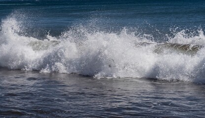 Dynamic ocean wave with foam and spray on the volcanic beach of Tenerife. Beautiful natural seascape showing strength, motion, and contrast of deep blue Atlantic water.