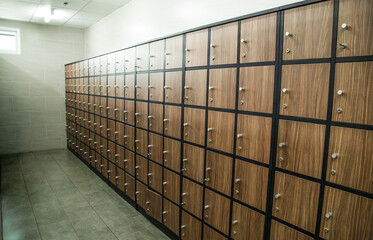 Wooden lockers with a wood bench in a locker room with doors closed. Locker room interior in modern fitness gym
