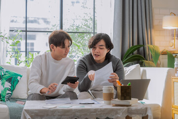 Asian LGBTQ male couple reviews monthly financial bills and household expenses together at home, managing shared budget planning, savings goals and responsible money management for their future 