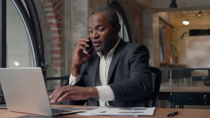 Multitasking African American business man talking phone check stats work laptop busy adult male executive businessman in office working with computer documents answering corporate call consulting - Powered by Adobe