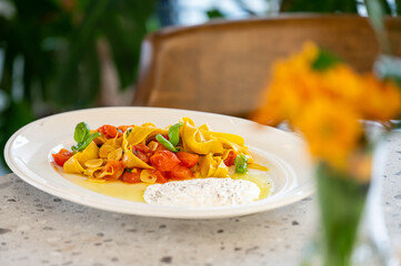 Plate of creamy pasta with cherry tomatoes and basil on a white dish, set on a speckled countertop with blurred flowers and greenery in the background, evoking a cozy dining vibe.