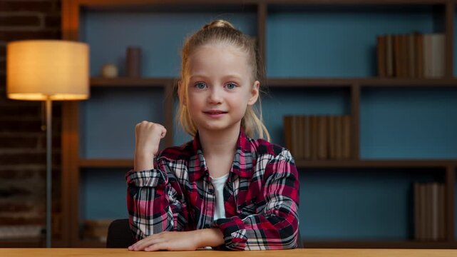 Caucasian little girl child kid daughter at evening home showing yes winning gesture overjoyed happy winner baby at table looking at camera win reaction achievement victory rejoice emotion achieve