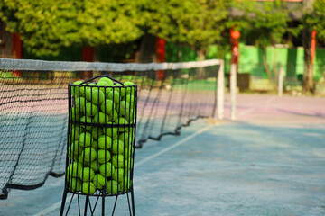 tennis balls collected in an iron rack with a tennis net in the background