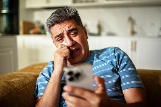 Middle-aged man crying while looking at phone