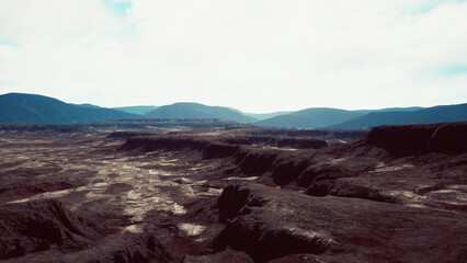 A vast expanse of rugged terrain stretches under a cloudy sky. The dramatic mountains rise in the background while deep valleys cut through the land, showcasing natures raw beauty.