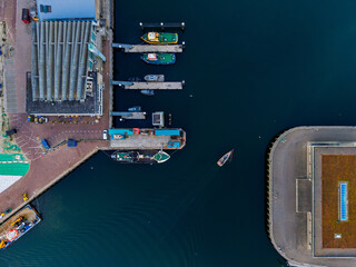Aerial view of harbor docks with moored boats, ridged-roof building, curved waterfront structure,...