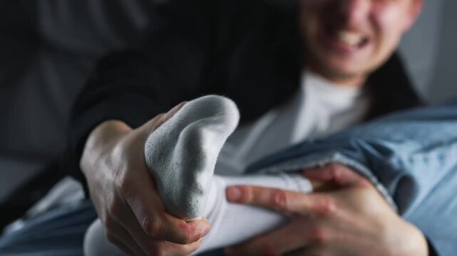 A young man has a foot injury.
A man hit his foot on a sharp object and is screaming in pain.
The man is holding his injured heel with his hand.
