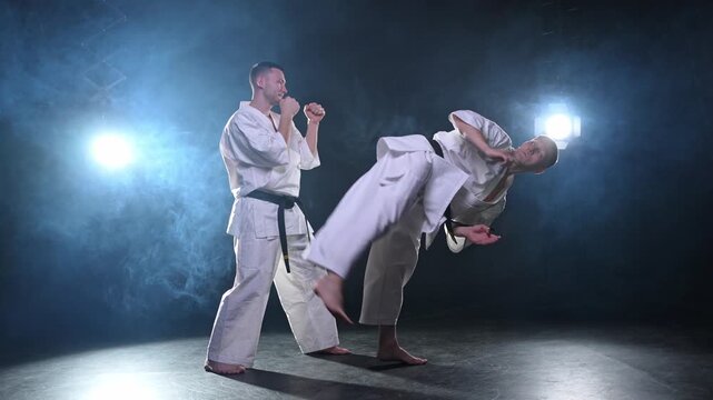 Martial arts masters on dark background. Strong man fighters in white kimono for karate martial arts fighting training in black gym. Karate fighters training punches kicks practicing fight sparring