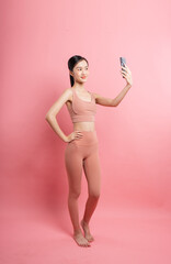 Fitness and fun: A young woman in exercise attire captures a selfie against pink backdrop