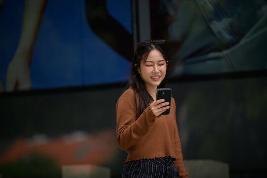 Young Asian woman smiling using smartphone outdoors - Powered by Adobe