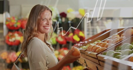 Smiling shopper in light blouse holding orange apple in produce aisle, graph overlay, copy space
