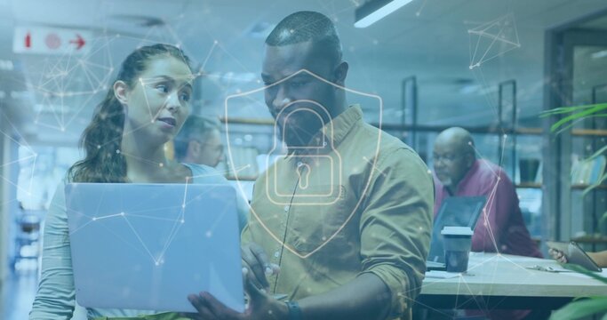 Collaborating Asian and African American duo examining laptop in shared office, security overlay