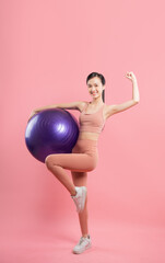 Smiling woman holding yoga ball exuding confidence and athleticism on pink backdrop Workout