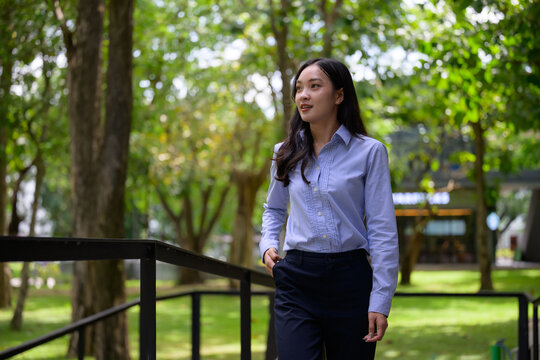 Asian businesswoman walking thoughtfully through green park