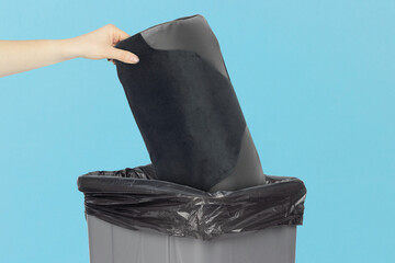 Throwing a chair back cushion for posture support into the trash, an outstretched hand with a chair back cushion for posture support in front of a trash can