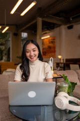 Fototapeta premium Asian woman remote working smiling using laptop in cafe