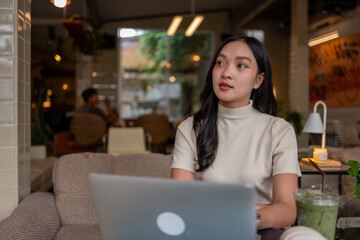 Fototapeta premium Thoughtful Asian woman using laptop working in cafe