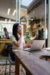 Asian woman making phone call working remotely in cafe