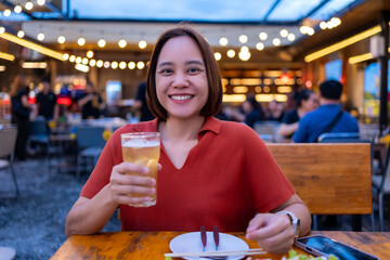 Smiling young Asian woman enjoying beer at restaurant