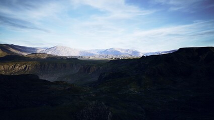 A breathtaking view of mountains stretches as the sun rises, casting soft light over rocky formations and deep valleys. The landscape showcases natures grandeur and tranquility.