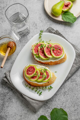 Sweet toasts with fresh figs, cheese, thyme, and honey on a gray background.